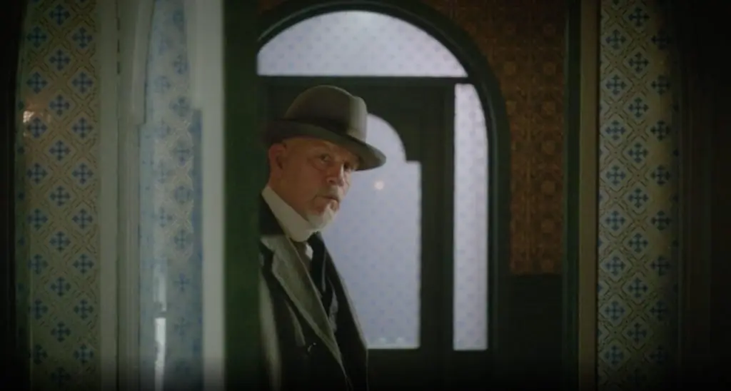 A man in a suit and hat is standing in a doorway.