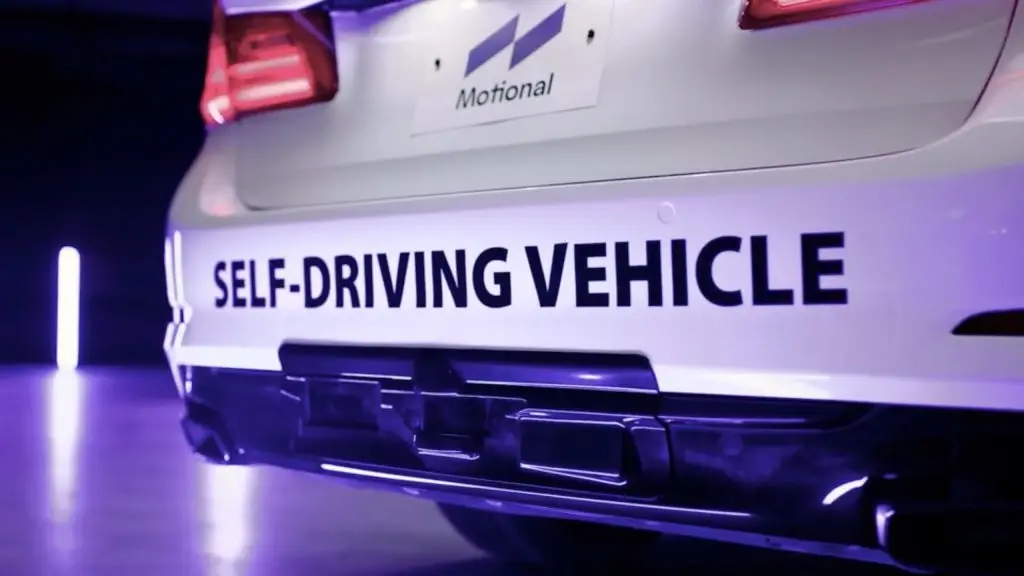 The rear end of a white car, showcasing a home decor-themed self-driving vehicle, is seen with the words "self-driving vehicle" prominently displayed.
