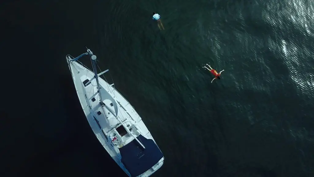 An aerial view of a person swimming in the water near a sailboat.