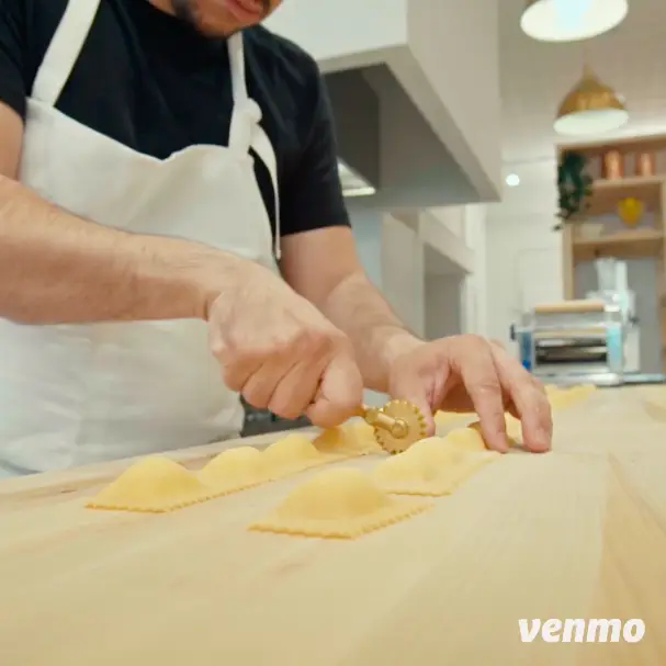 A man is preparing ravioli on a wooden table for his online community.