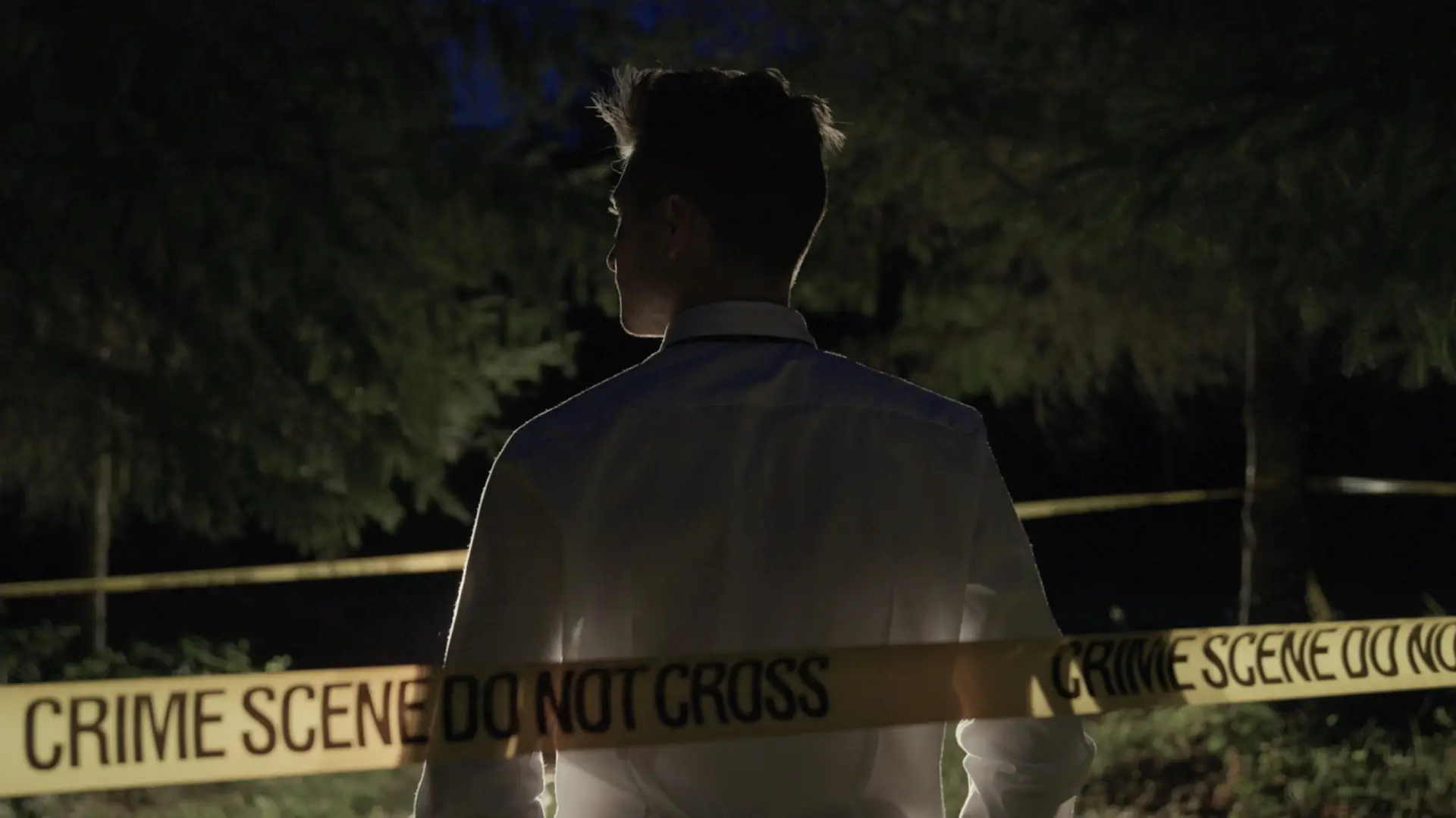 A man standing in front of a crime scene tape at night, involved in crime investigations.