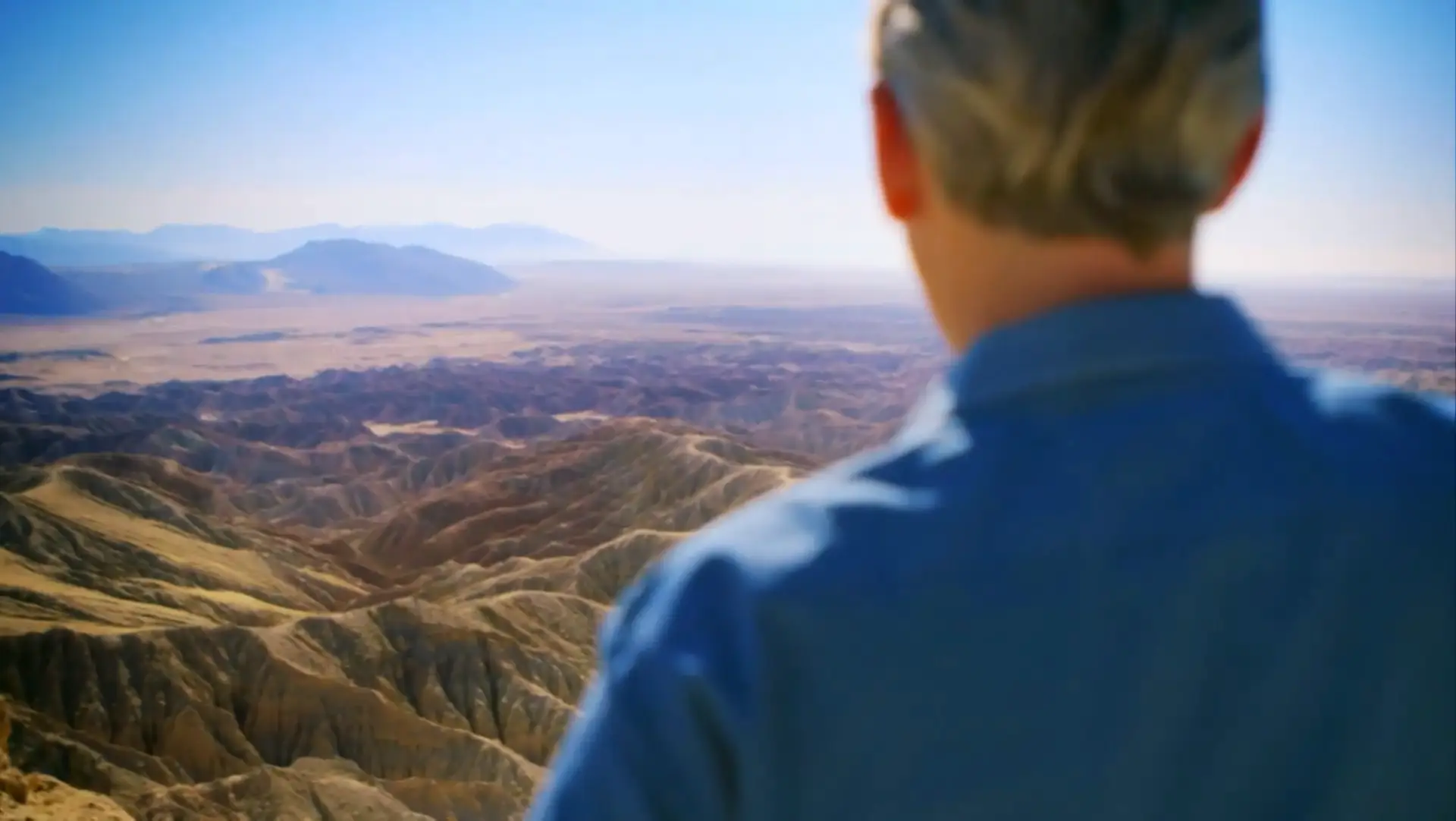 A man is standing on top of a mountain overlooking a valley, featuring breathtaking views.