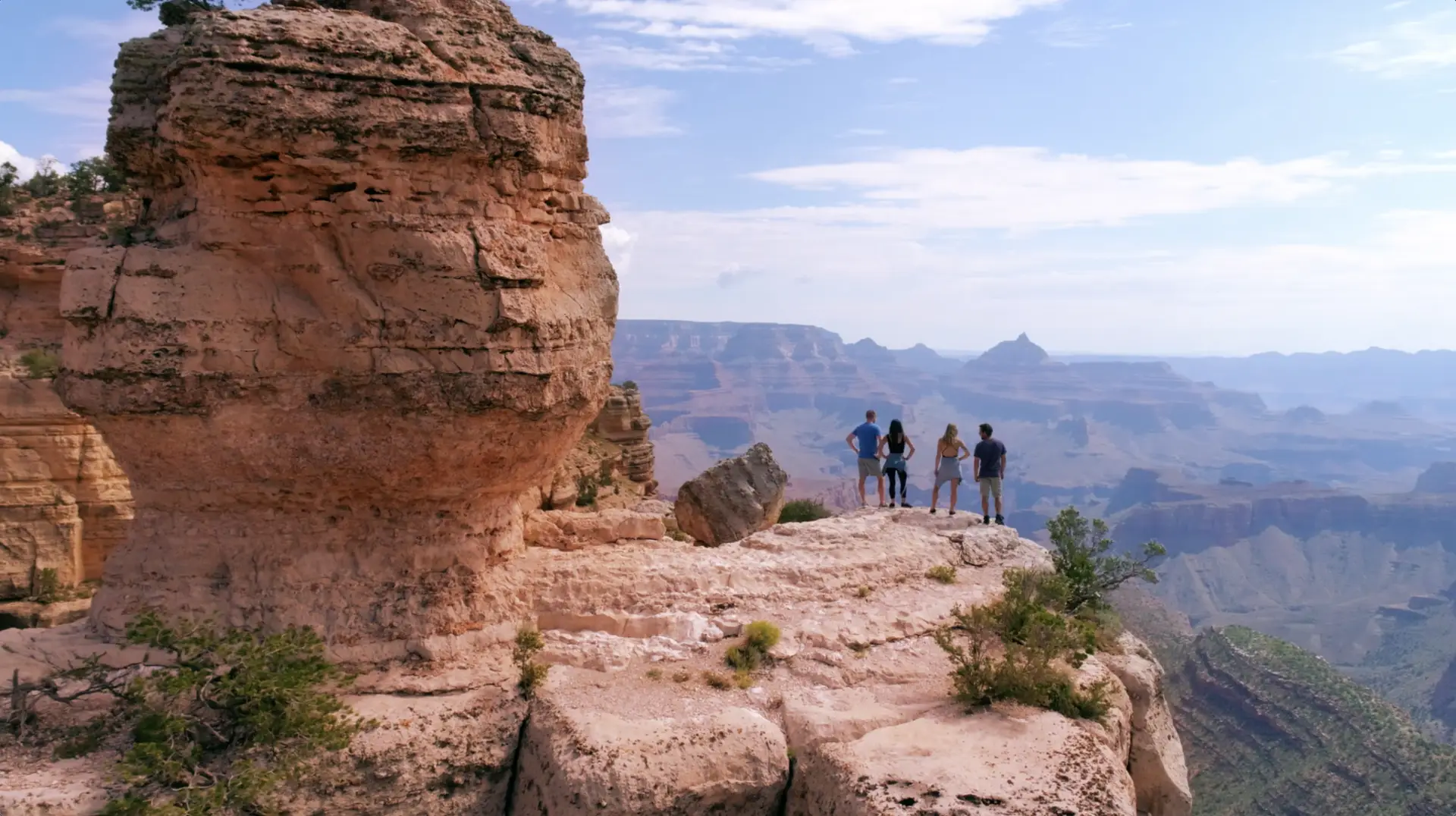 A group of people are standing on the edge of a cliff, overlooking the grand canyon during their AAA trip.