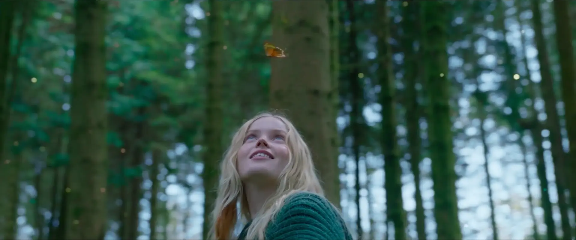 A girl is standing in a forest with a butterfly flying in the air, in December.