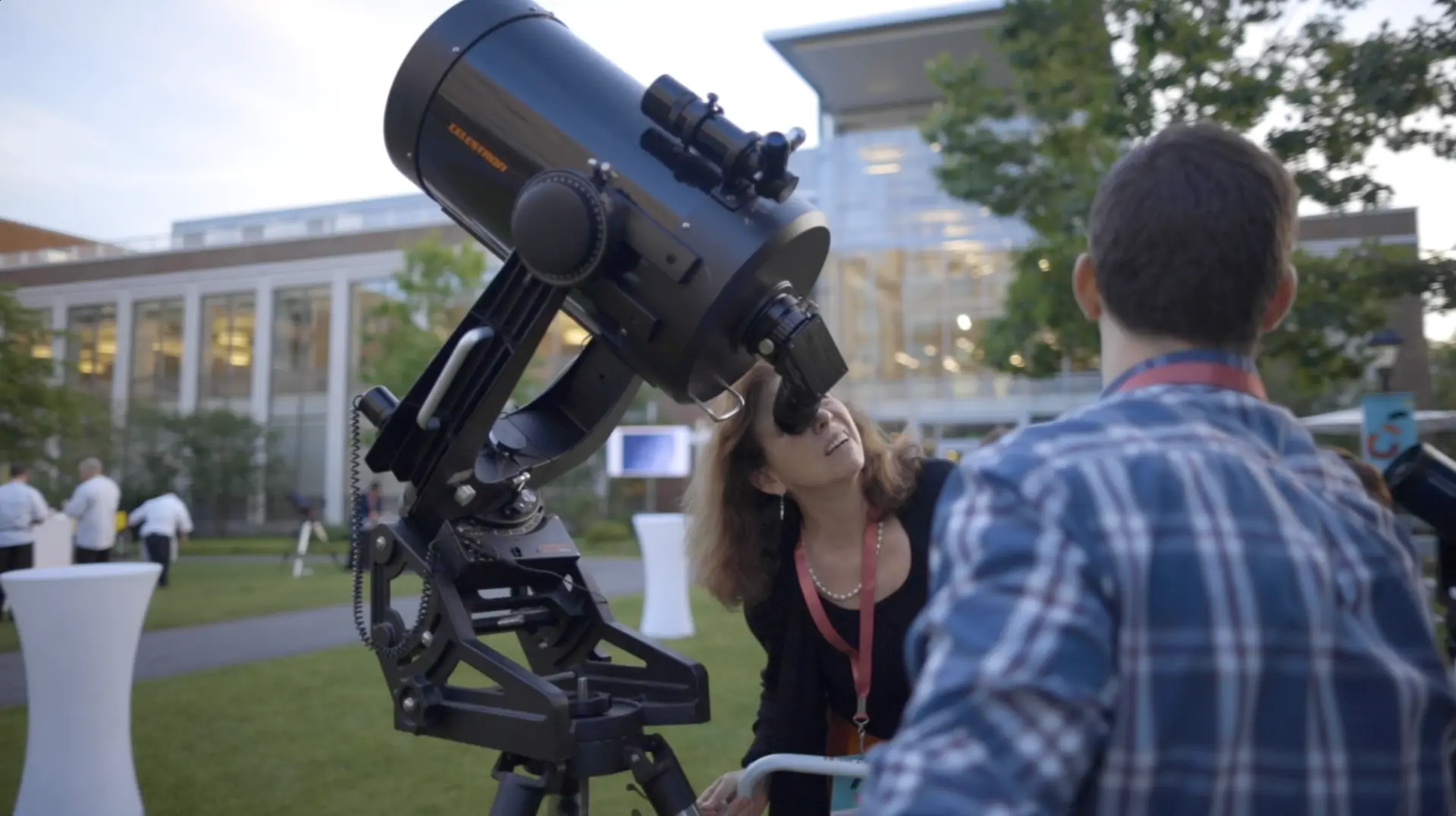 Two people looking at a telescope in front of the Harvard Business School building.