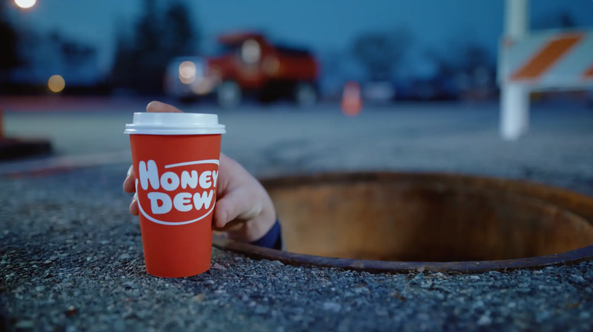 A person holding a Honey Dew coffee cup out of a hole in the ground.