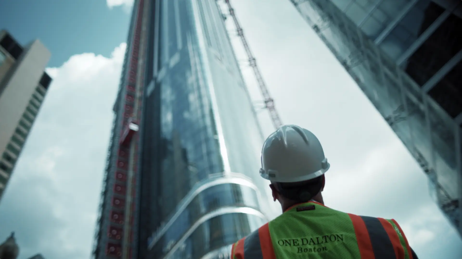 A construction worker is standing in front of a tall building for an NBC Boston image spot.