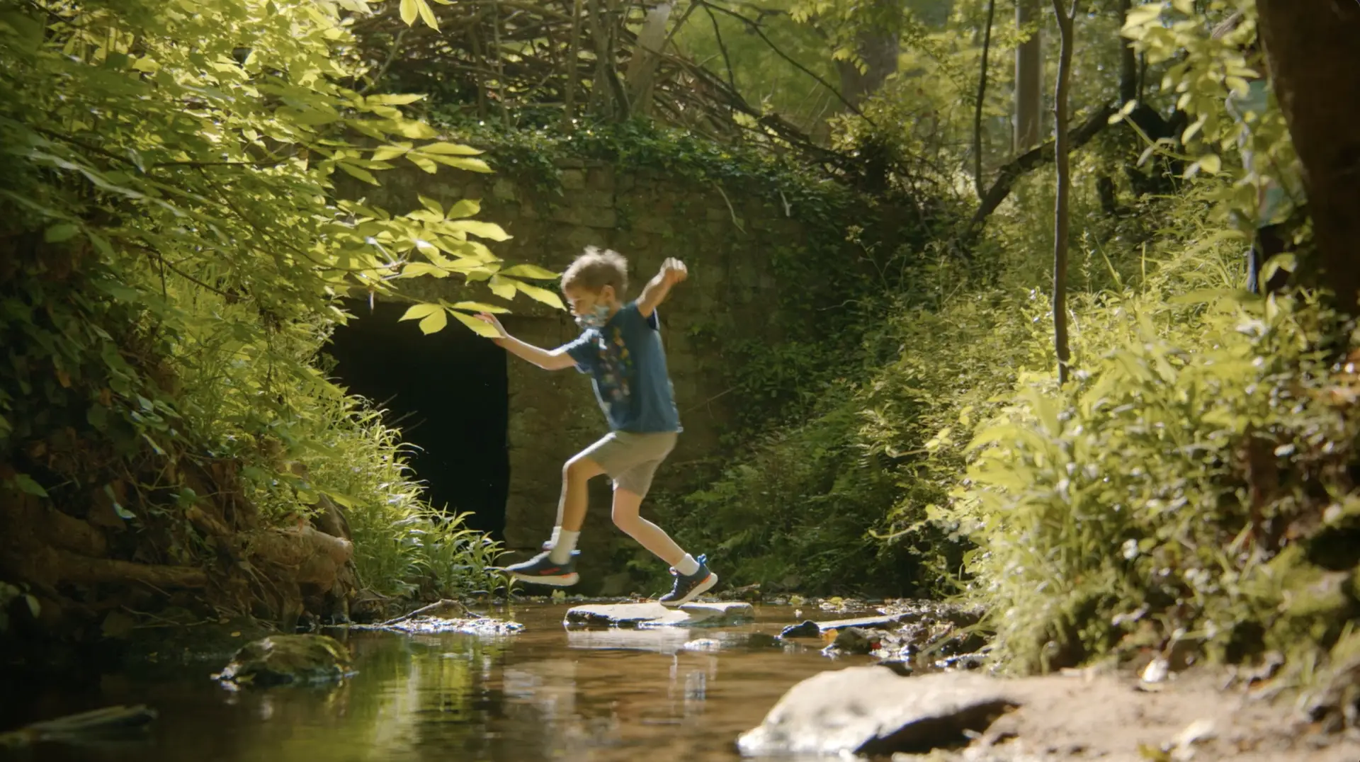 A boy jumps over a stream in the woods, an act seen in many stories.