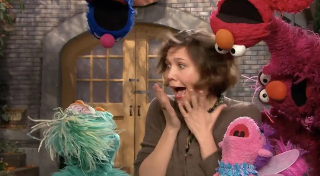 A woman entertains a group of sesame street puppets.