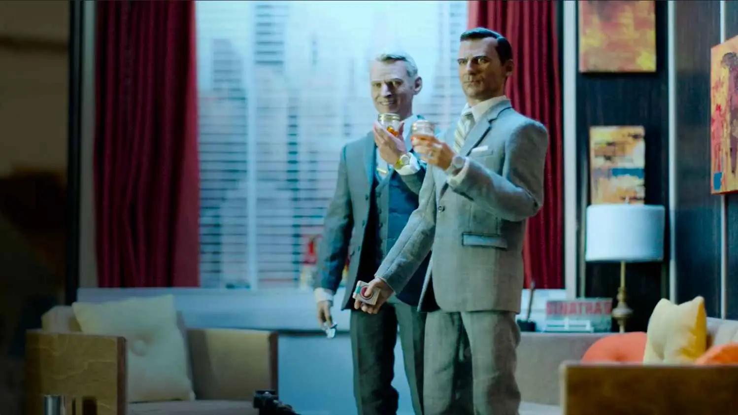 Two men dressed in suits holding drinks, standing in a room with urban views through the window, surrounded by an array of sales material.