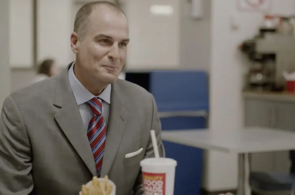 Man in a suit with a fast-food meal smiling in a restaurant setting, enjoying his Hulu streaming service.