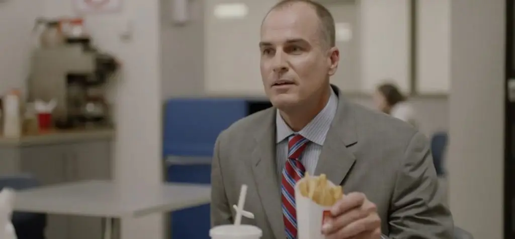 Man in a suit sitting in a fast food restaurant with a carton of fries, browsing through his sales content library.