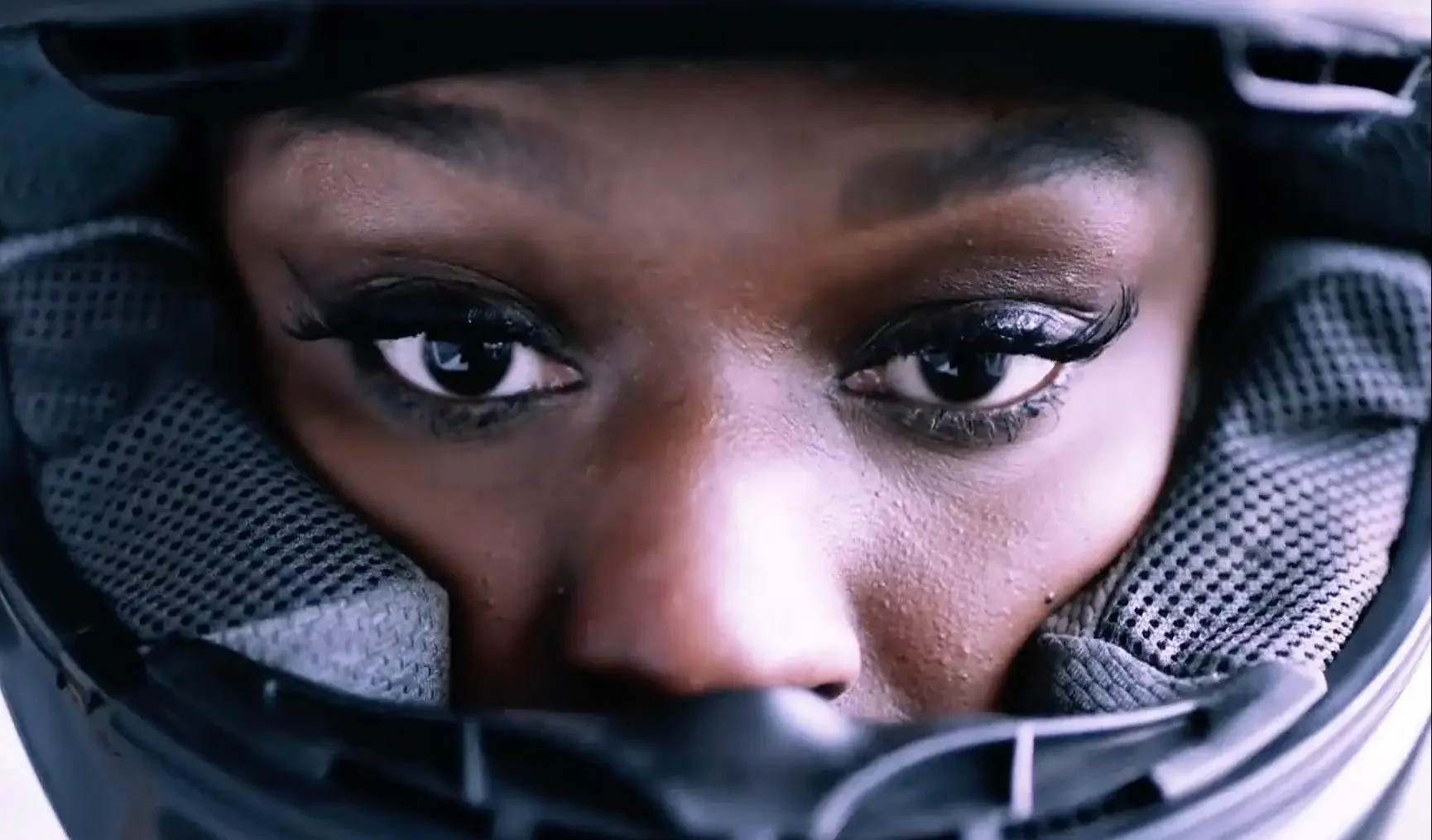 Close-up of a woman's face wearing a black motorcycle helmet, focusing on her eyes visible through the helmet's sales content library.