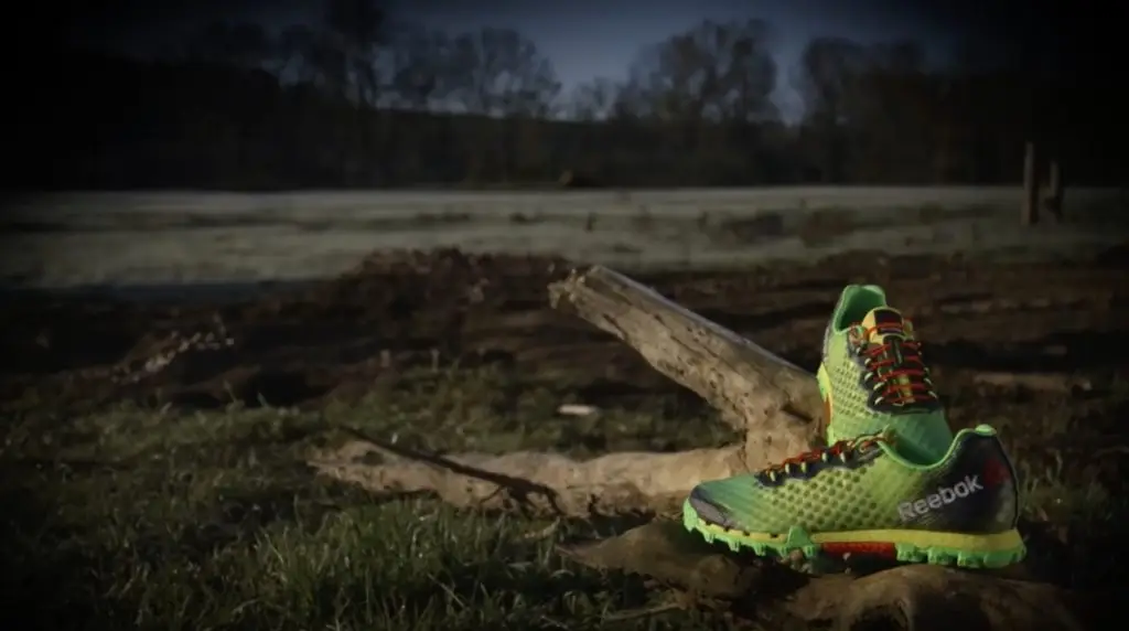A single green Brooks sneaker positioned on rough ground with a frost-covered field in the background.